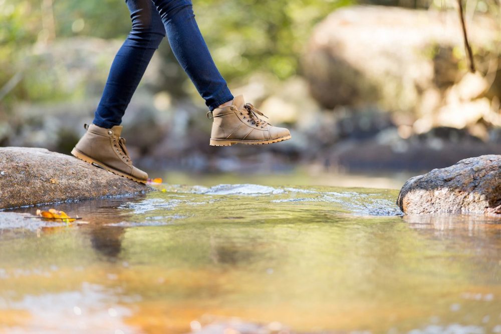 Beine einer Person in Wanderschuhen die versucht einen Wildbach zu überqueren