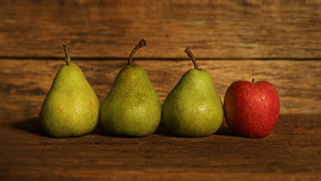 Drei grüne Birnen und ein roter Apfel in einer Reihe