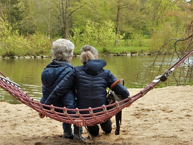 Eine Seniorin im Sessel wird von einer Frau von hinten umarmt